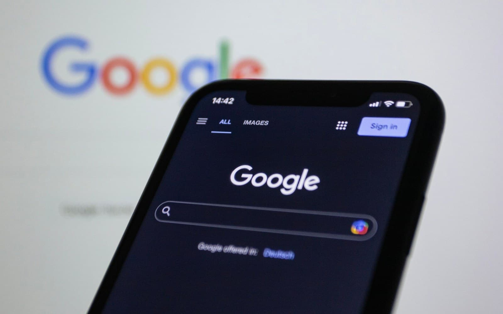 Primer plano de un móvil con la app de Google abierta, con el logo de Google desenfocado al fondo